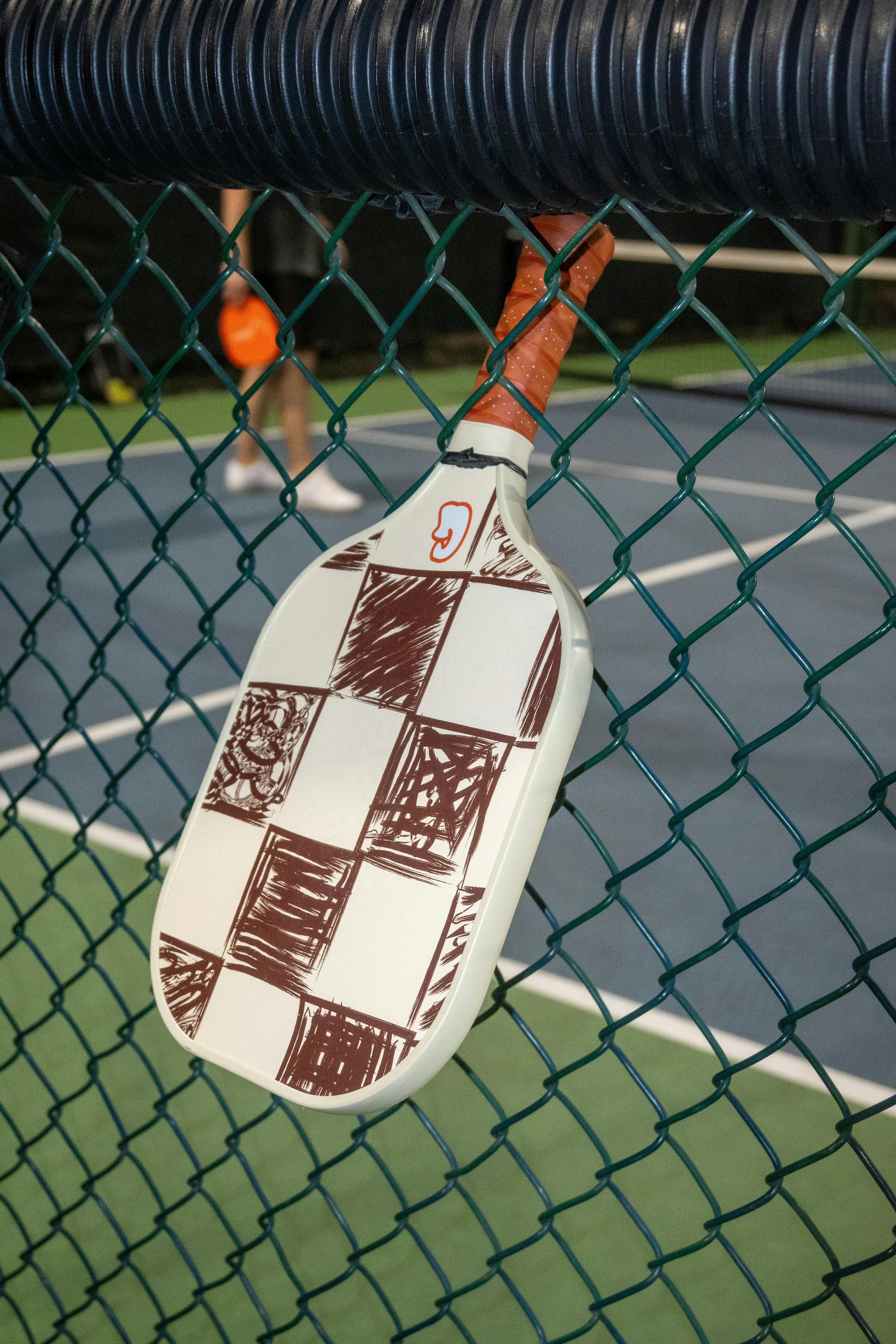 Pickleball paddle hanging on court fence at night